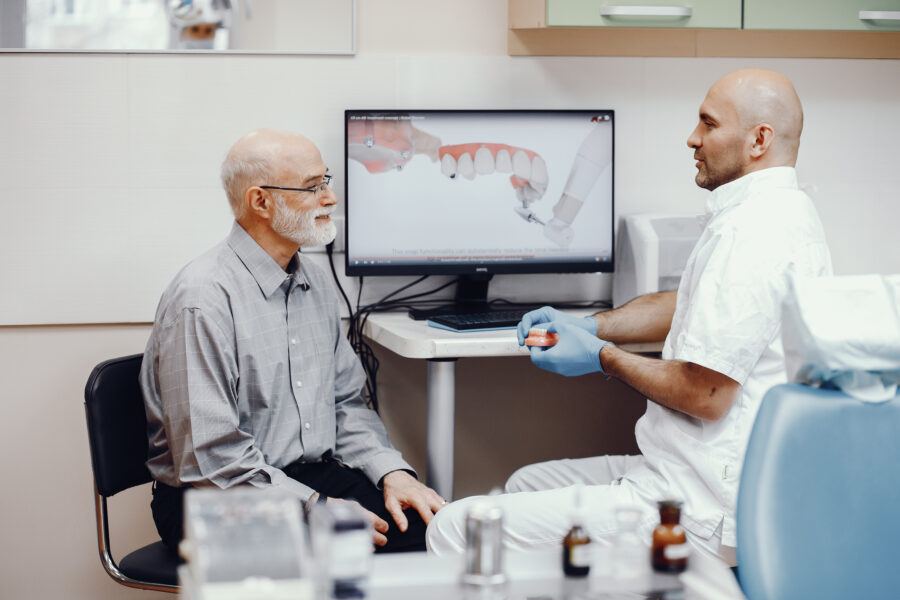 cirurgião dentista informando as contraindicações para implantes ao seu paciente senhor de idade.